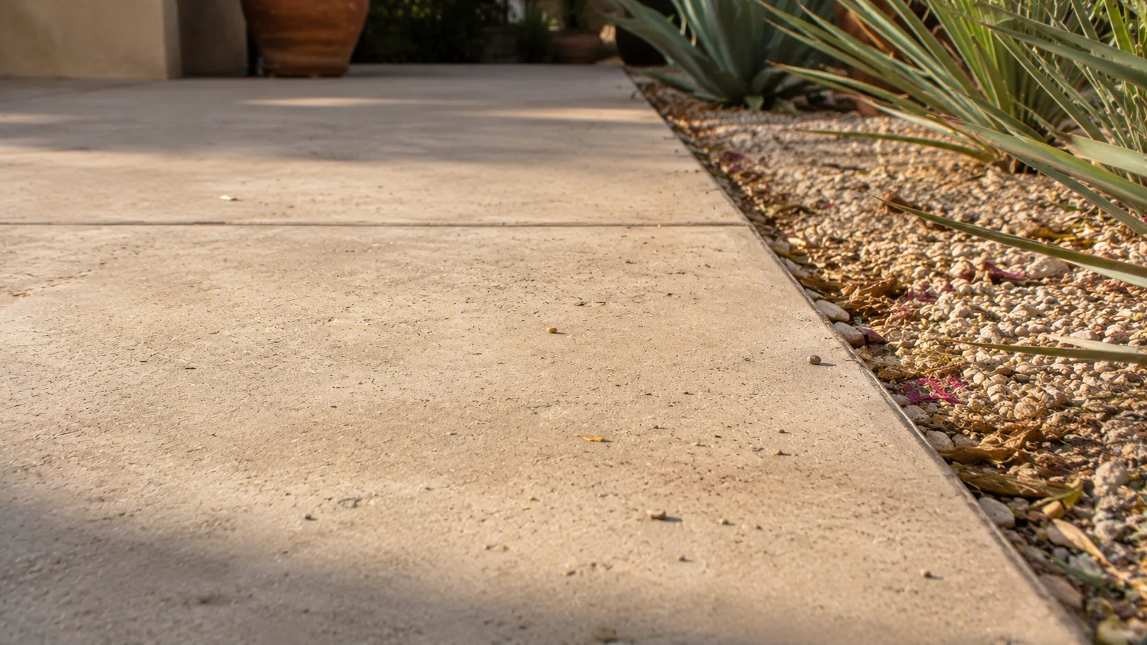 Close-up of outdoor concrete patio texture and edge detail where the slab meets gravel and planting.