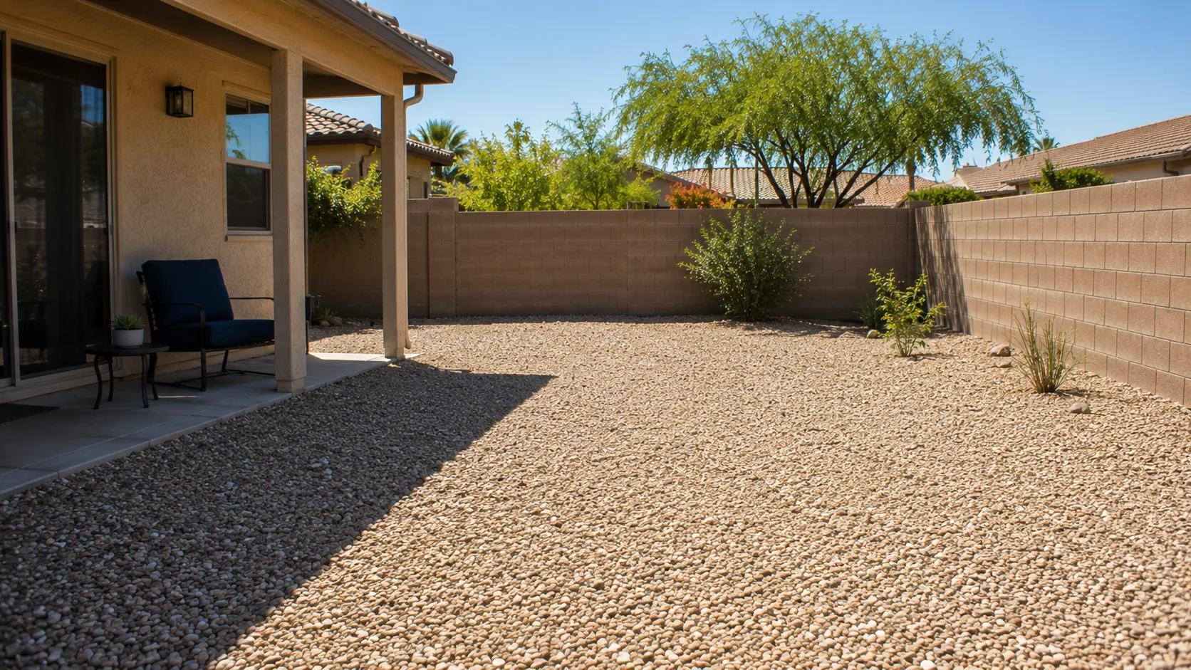 Exposed gravel backyard with bright hardscape glare, sparse planting, and limited shade.