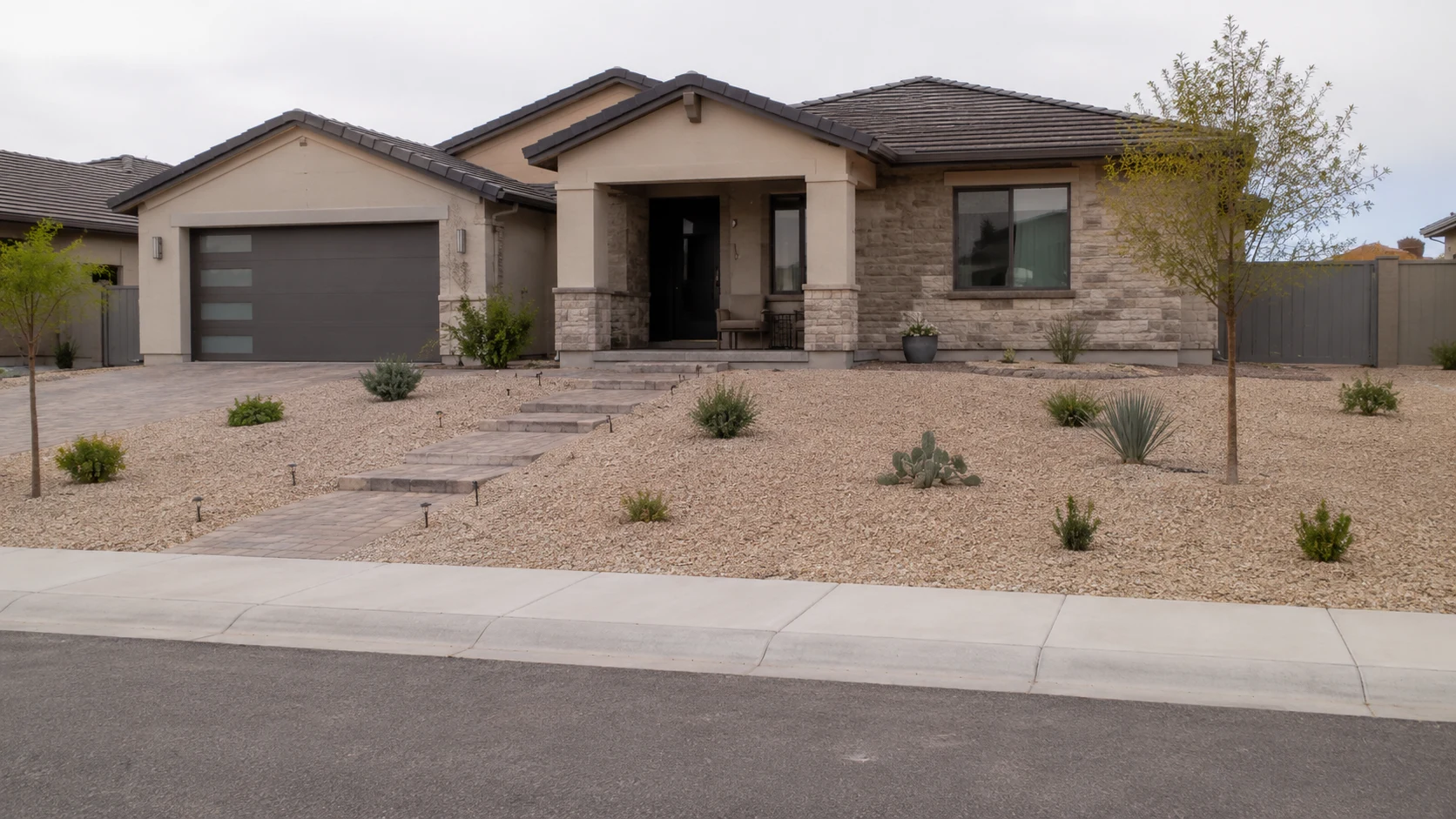 Sparse low-water front yard with too much exposed gravel and small isolated plants.