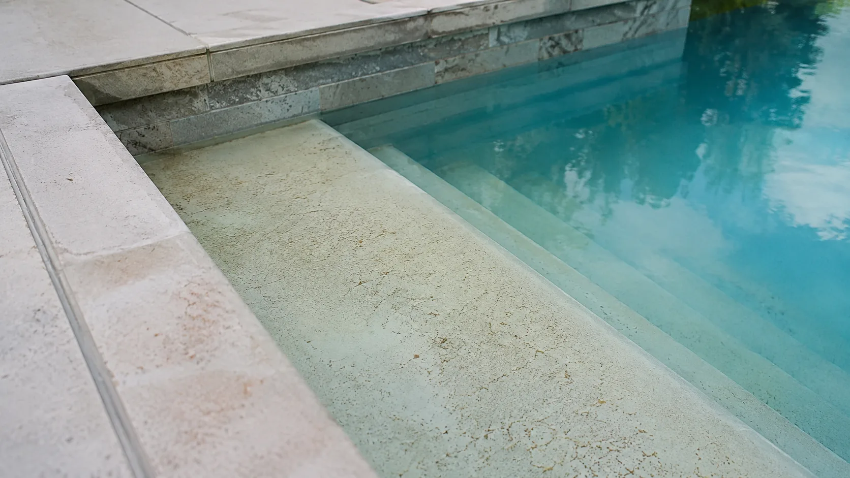 Fine tan dust settled on pool steps and a shallow ledge after a dry wind storm.