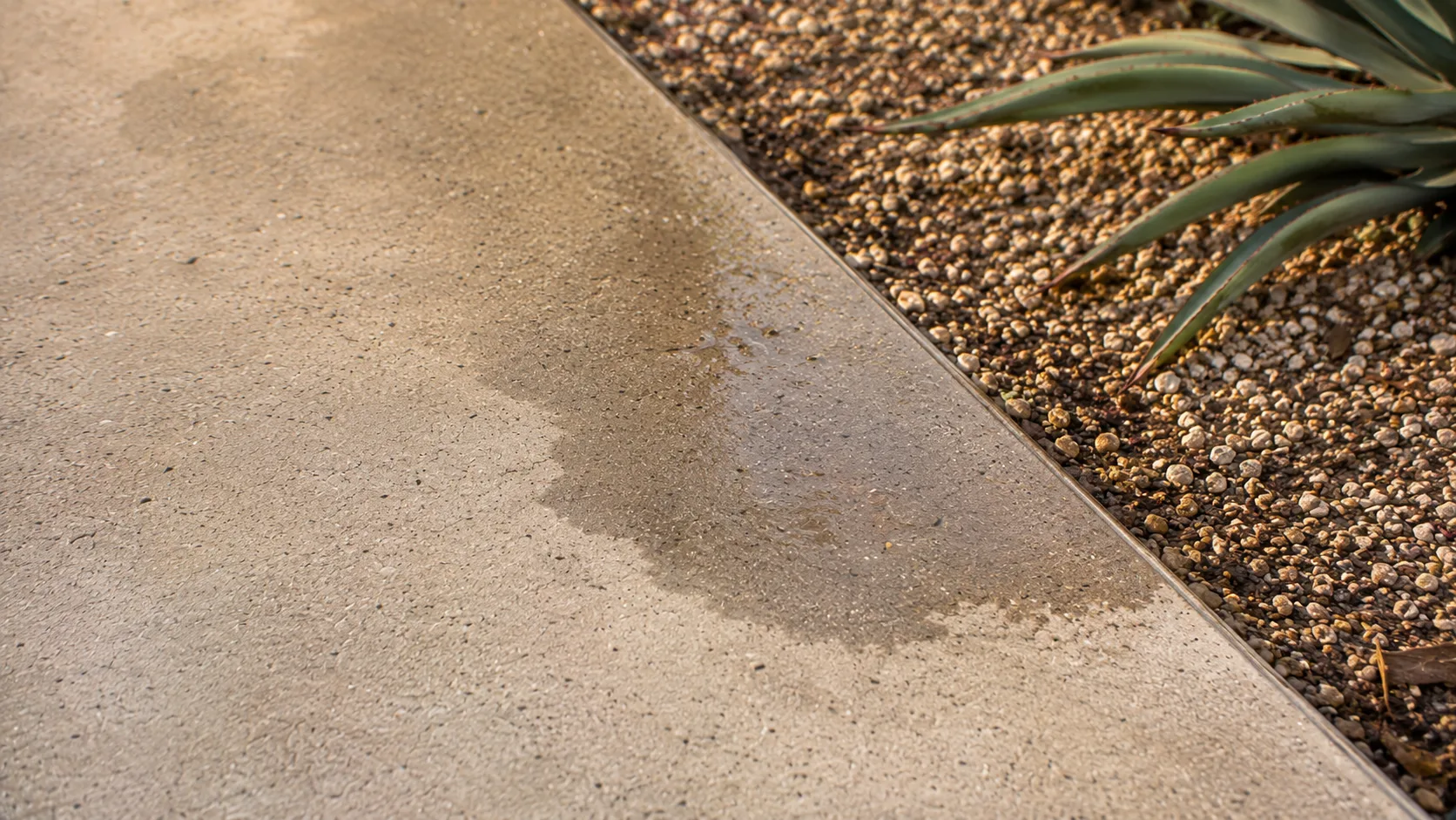 Close-up of outdoor concrete surface texture and subtle uneven drying near a gravel edge.