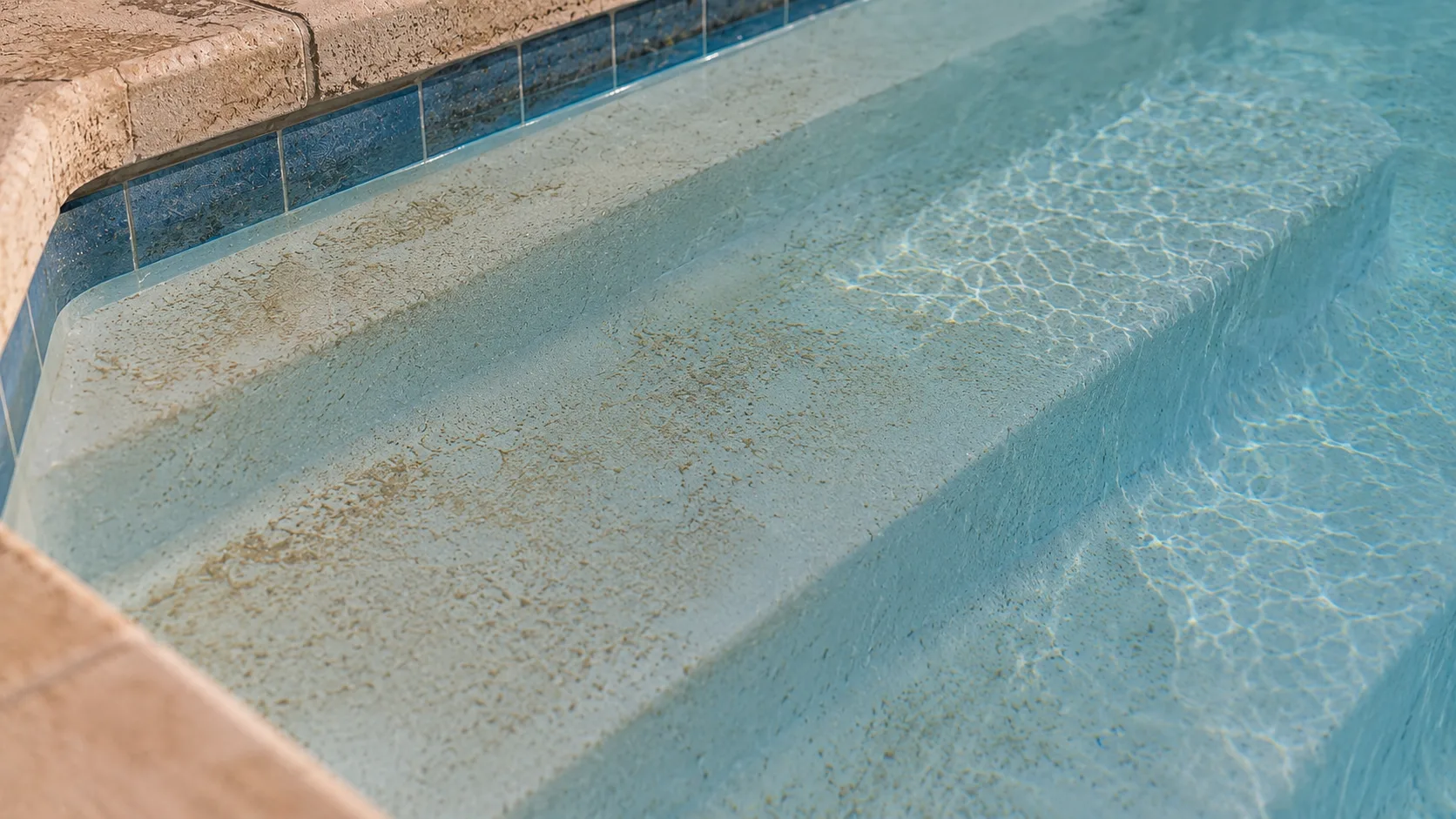 Fine tan dust lightly resettled on pool steps after a robotic cleaner run.